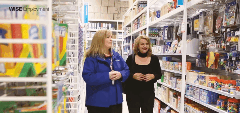 Two women walking down the aisle of an officeworks store, smiling.