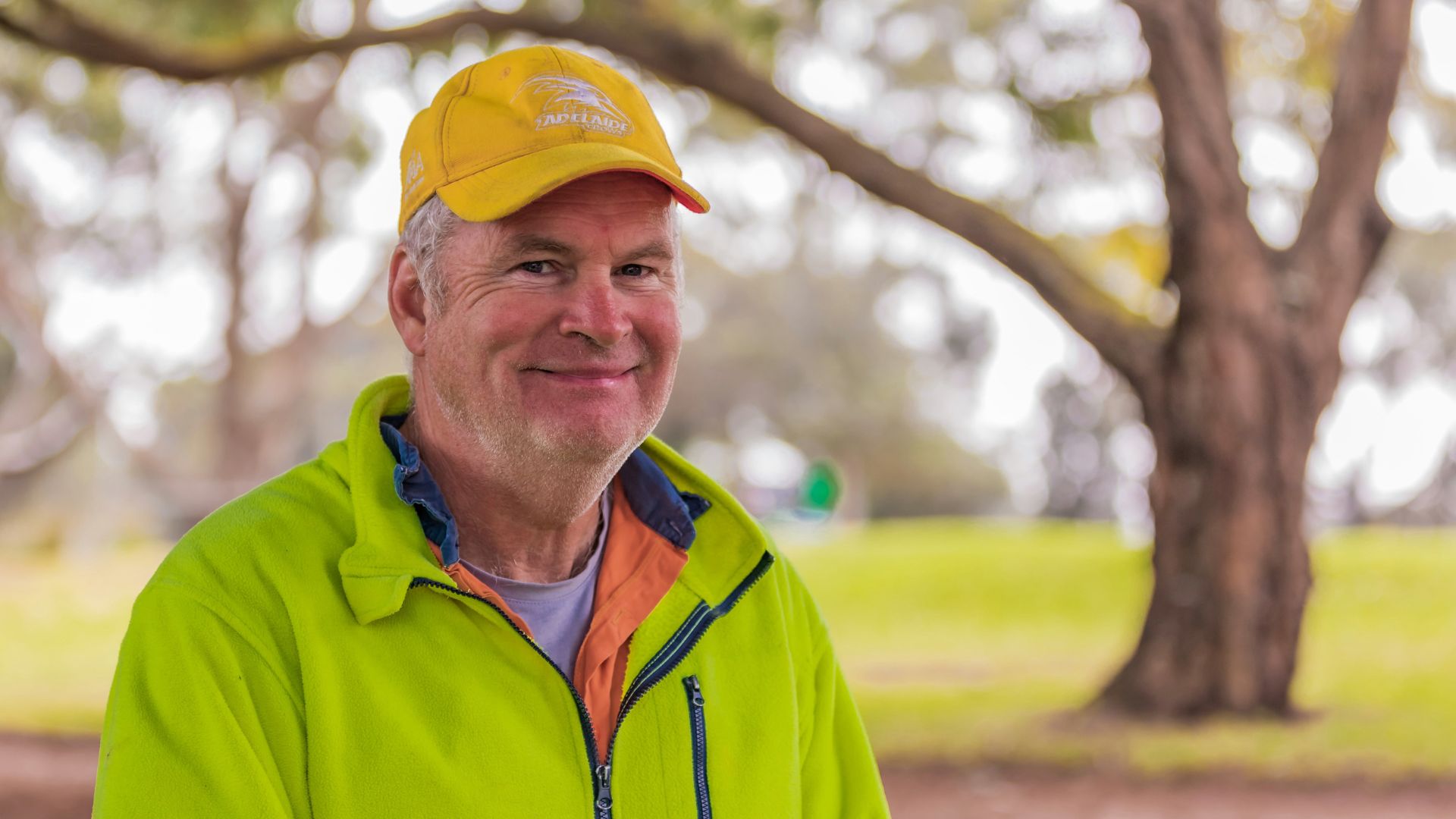 Grant is in his high-vis jersey and yellow hat standing outside on the golfing grounds. He is smiling at the camera.