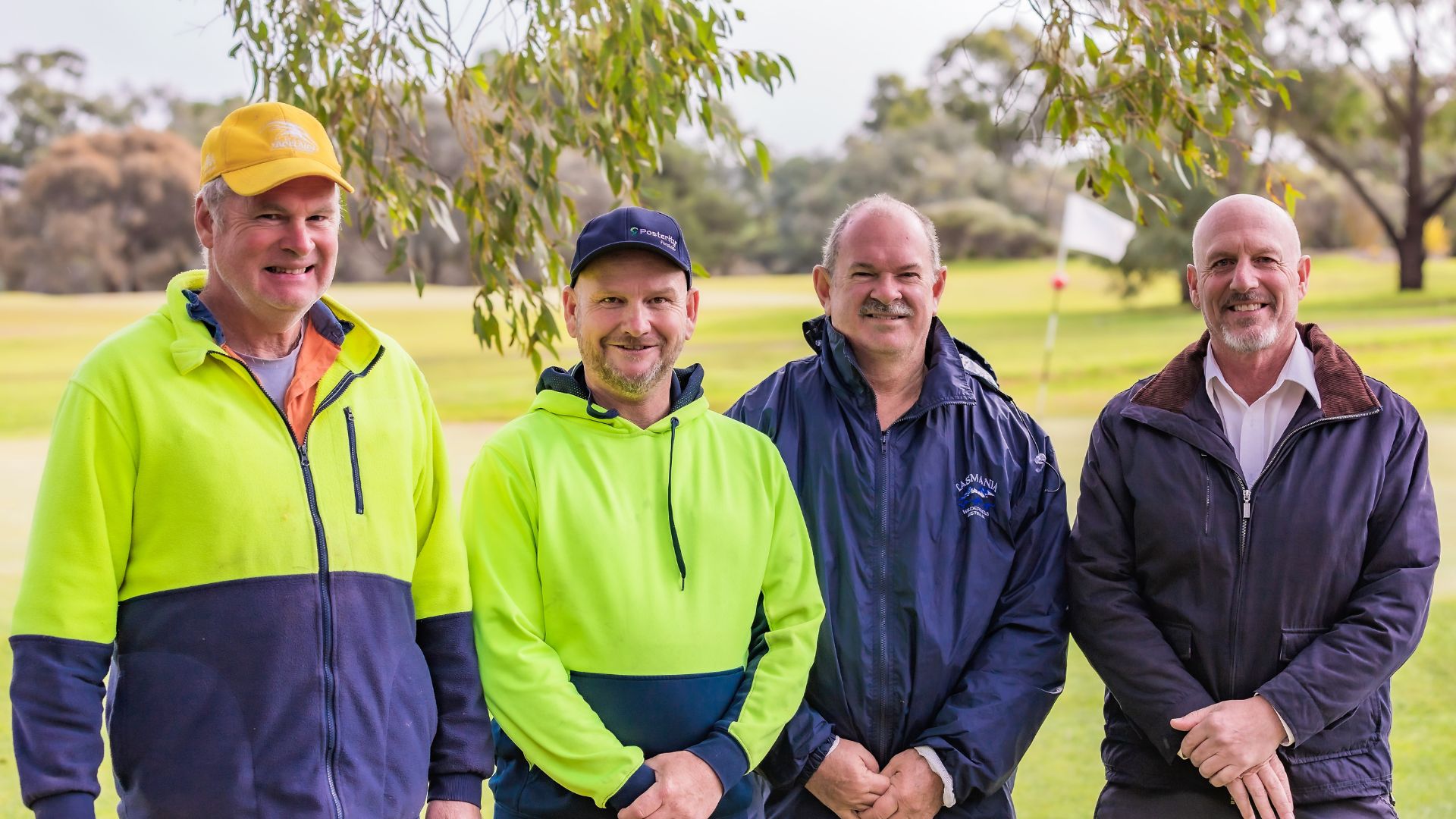 Grant stands beside his support worker Grant, Employment Consultant Brenton and Superintendent Andrew. They are all standing on a field.