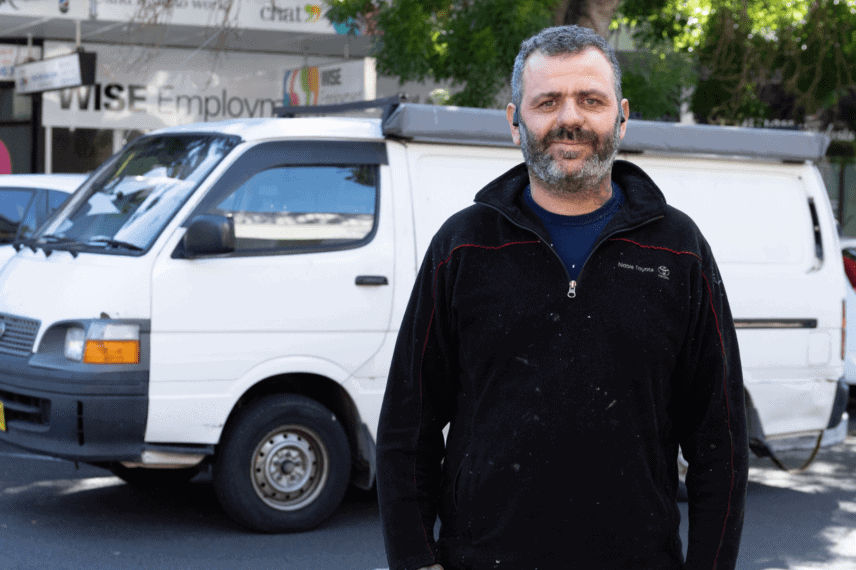 Abed standing in front of work van