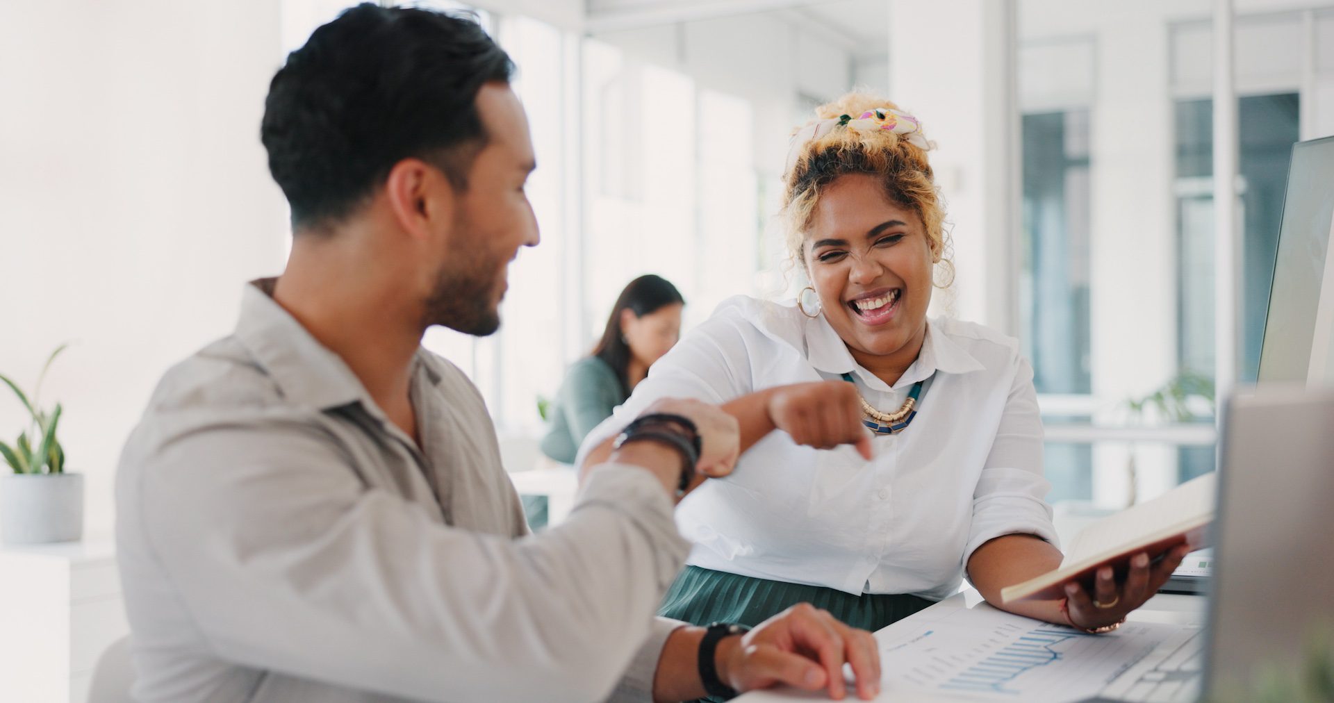Happy employees fist bumping in celebration of achieving sales goals at an office desk, representing teamwork and success.