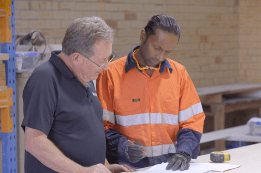 A South Asian machine worker going over designs with his senior manager.
