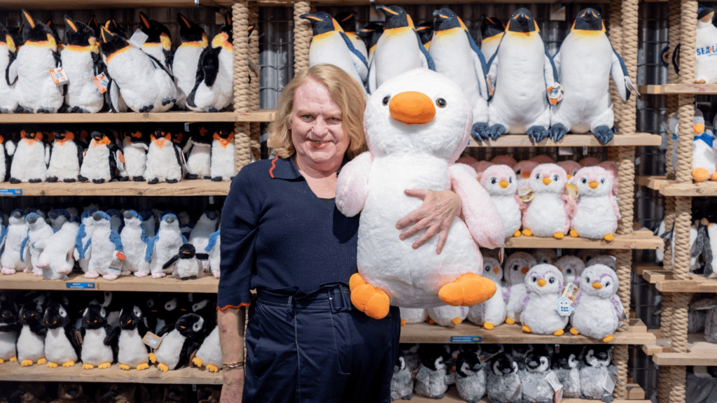 Bianca standing in front of shelves of plush toys, holding a large penguin plush toy in her left arm