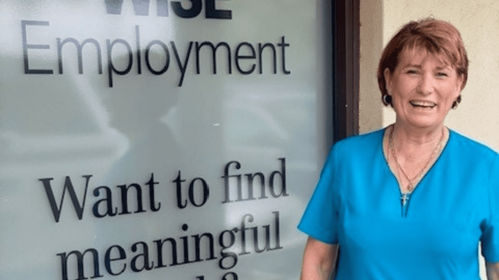 A smiling middle-aged woman smiling in front of an employment office.