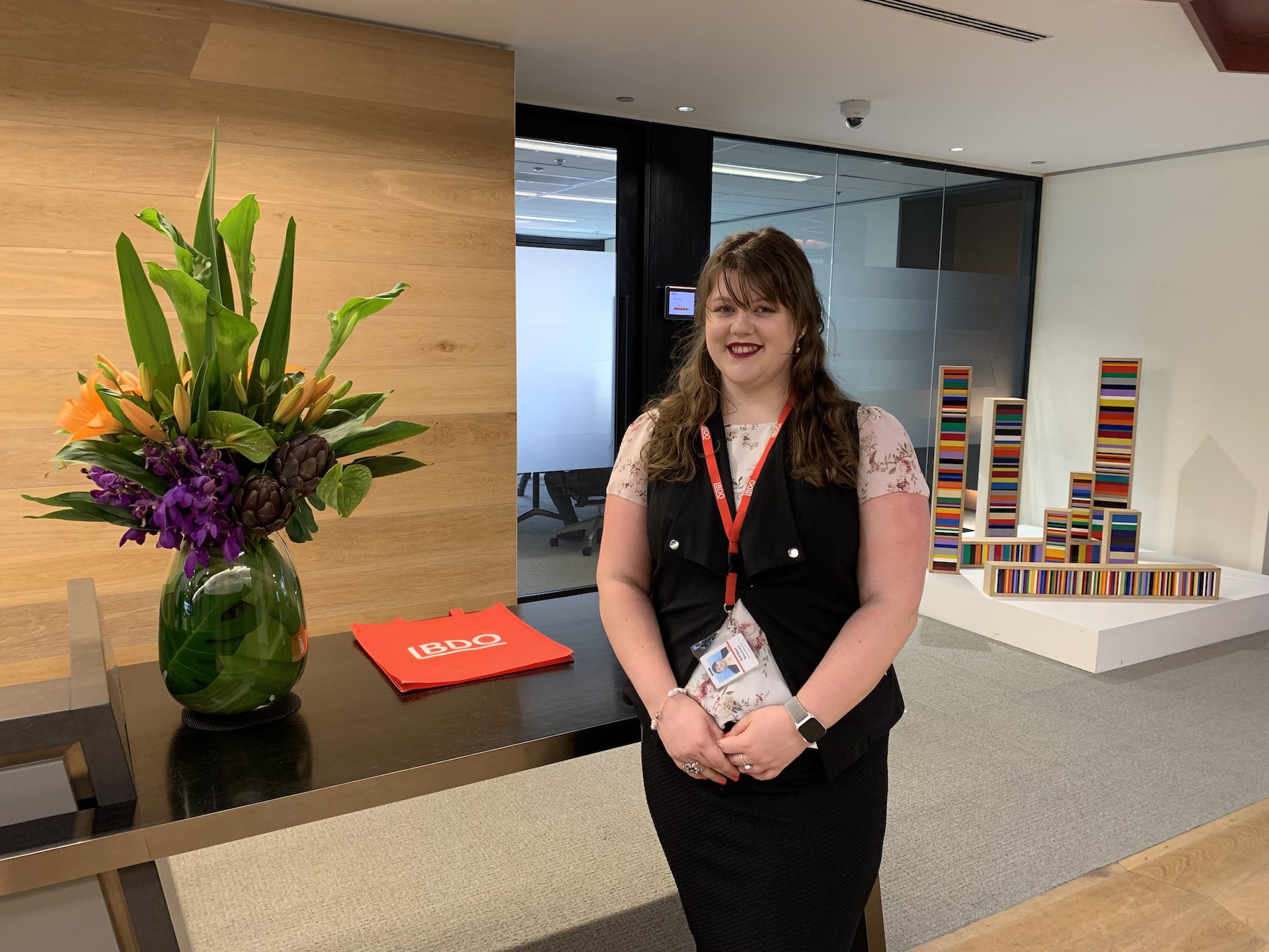 Smiling woman, standing in front of an office reception desk.