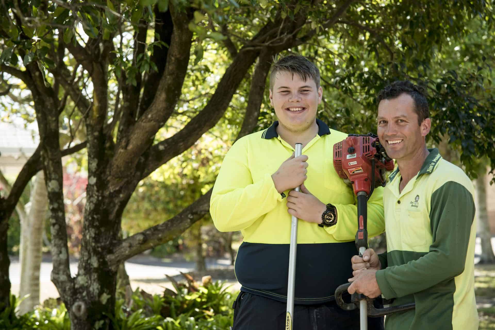 Two men holding leaf-picking tools in front of a tree.
