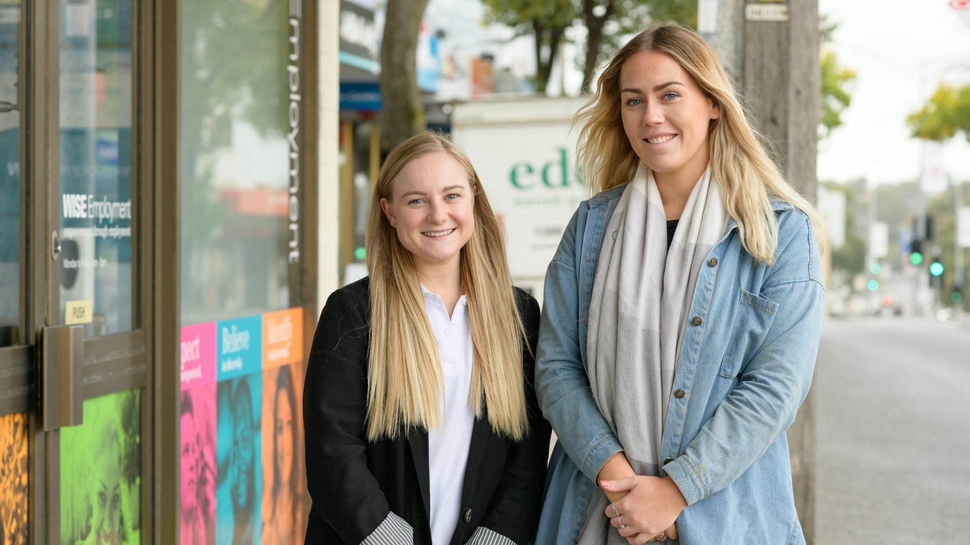 Two smiling women standing outside an employment office.