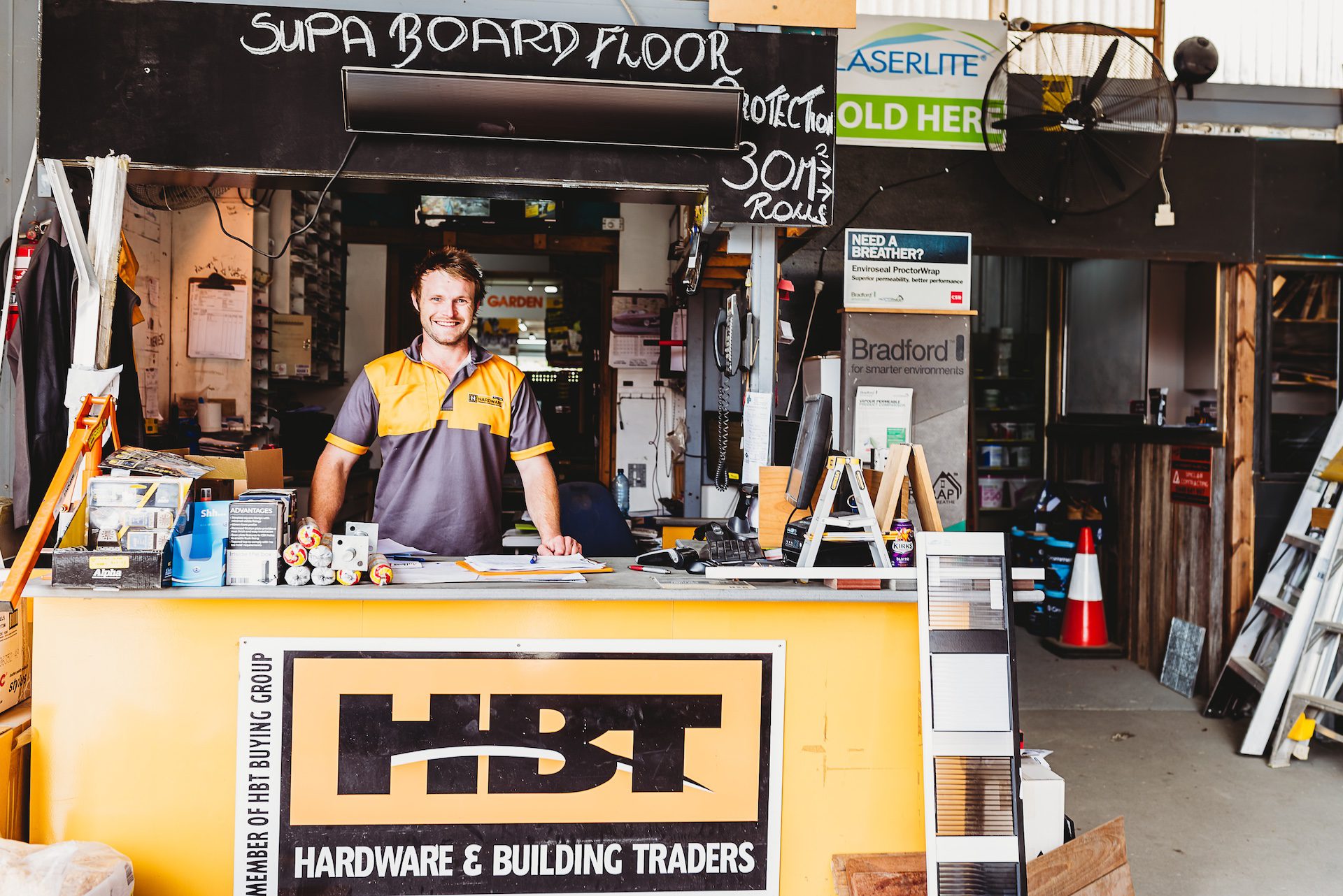 A young man smiling while standing behind the counter of a hardware store.