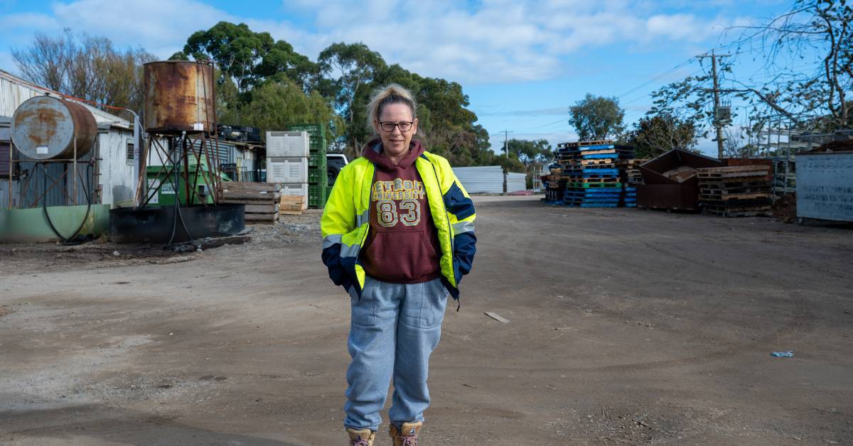 Kylie is wearing a yellow hi vis jacket, standing outside in a workyard