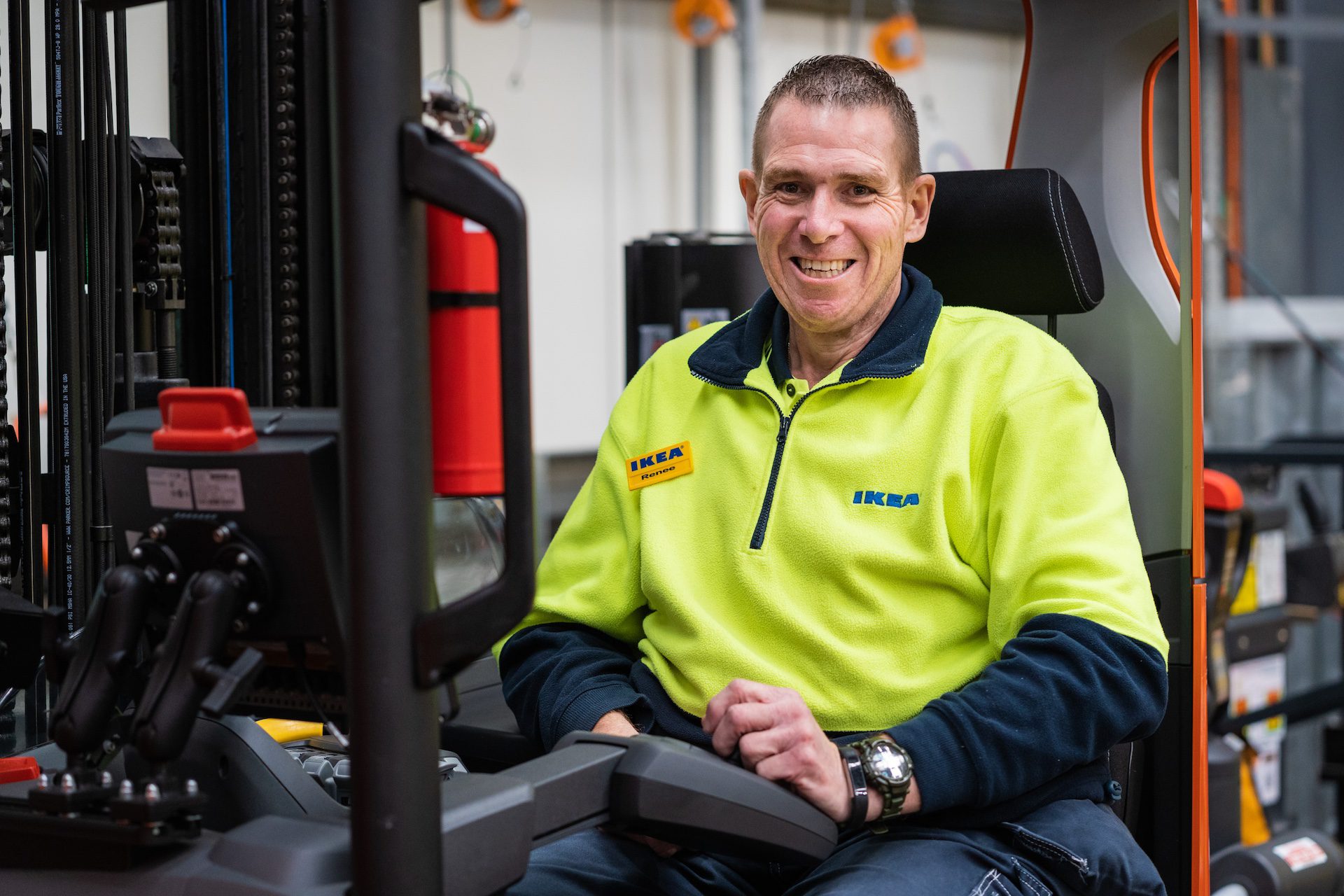 Elder man in an Ikea uniform, smiling while sitting in a forklift.