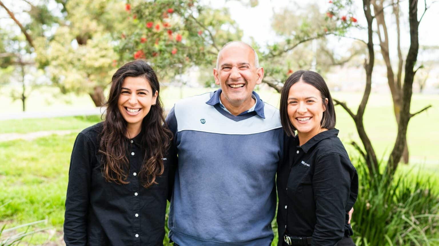 Man and two women smiling, standing in the park.