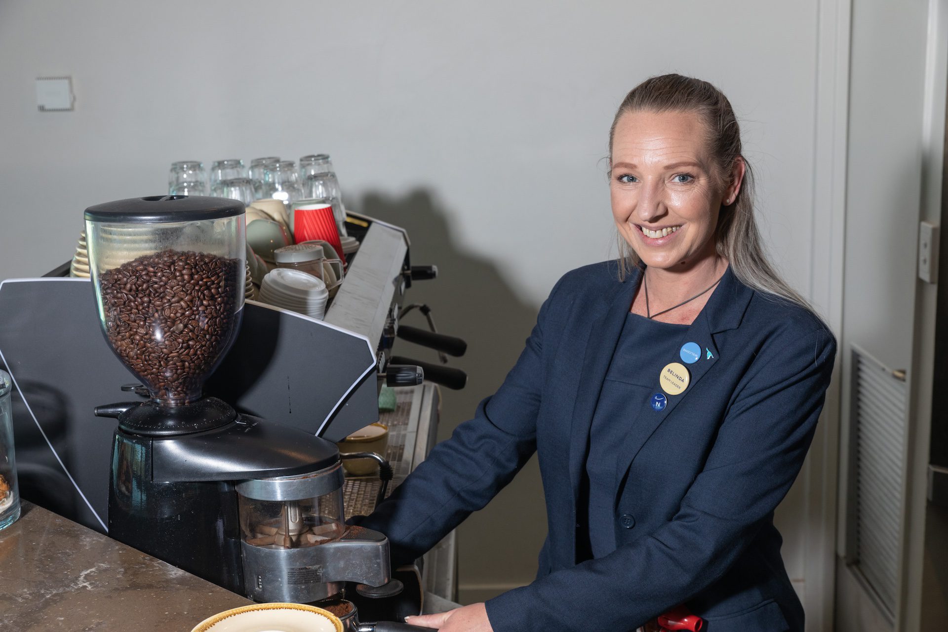Woman smiling as she stands beside a coffee machine.
