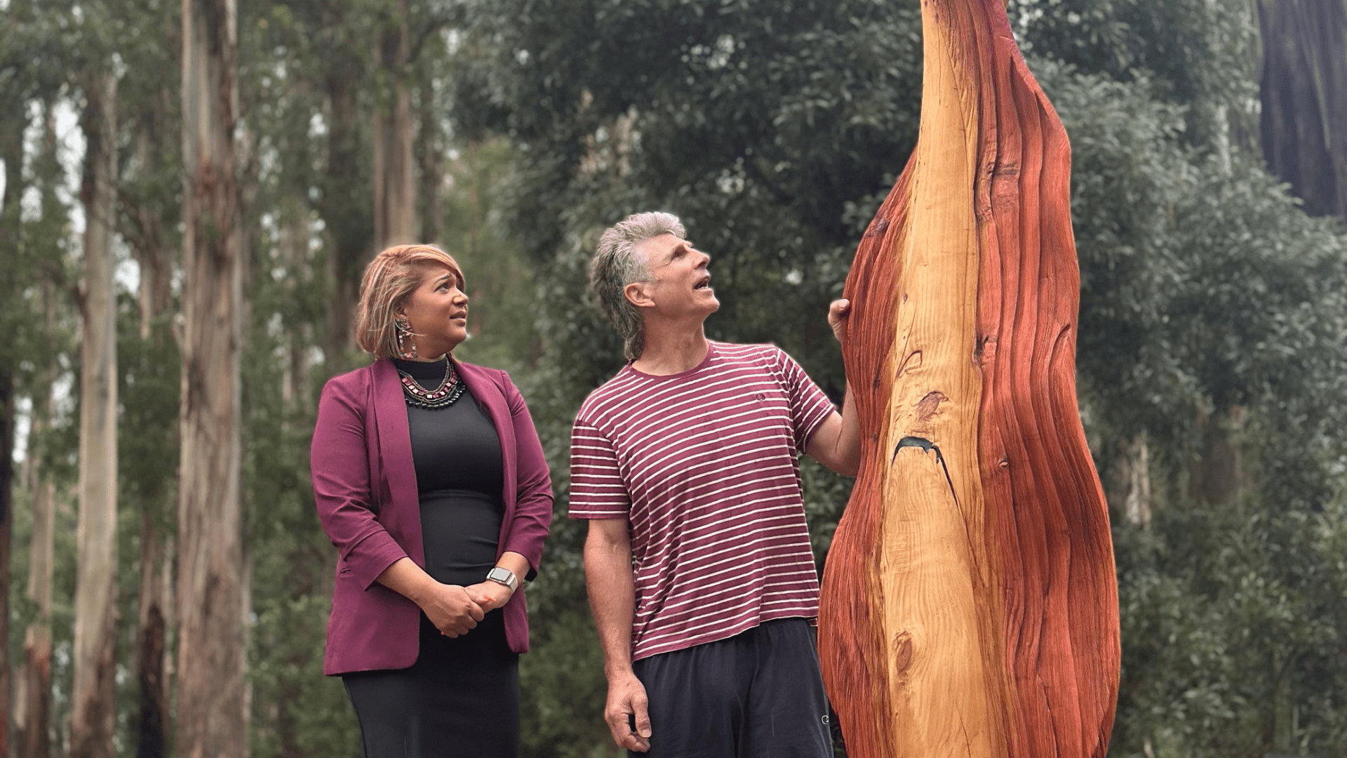 Anton standing outdoors with case manager Laurianne, next to a large wooden sculpture Anton created