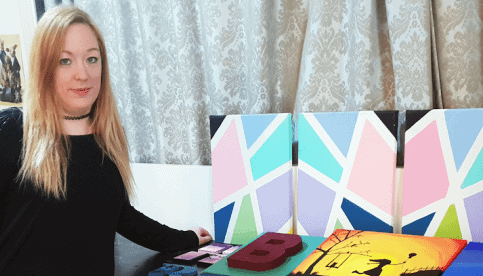 A young womanstanding beside a colorful artwork.