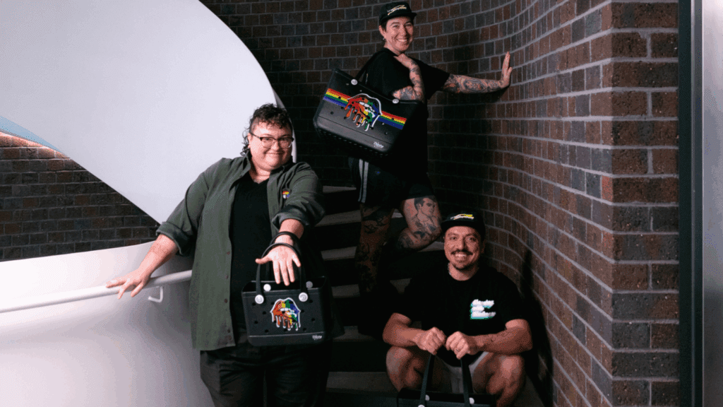 A man and two women happily posing while holding merch bags on a stairway.