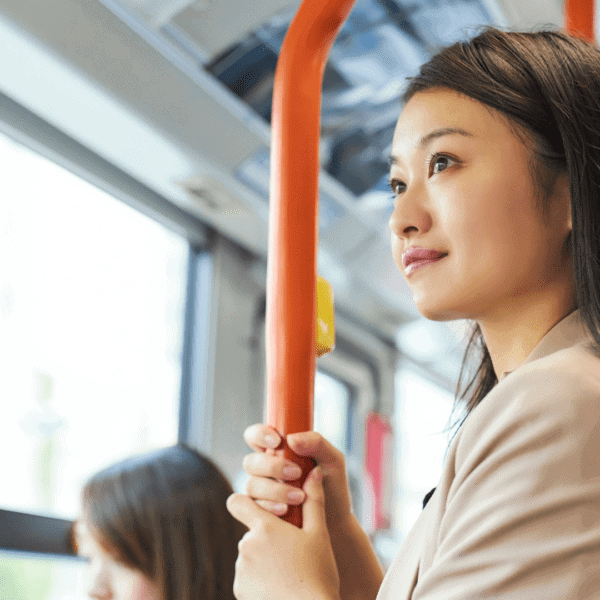 A woman standing on public transport, holding a handrail and looking out the window.