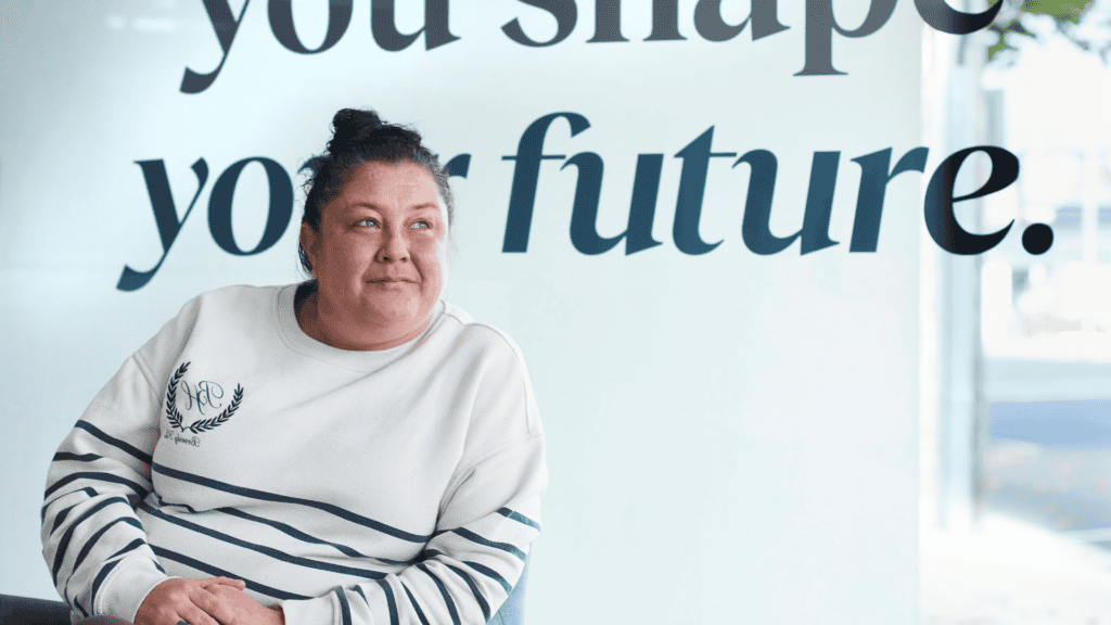 A woman sits indoors looking up, with the words “you shape your future” behind her.