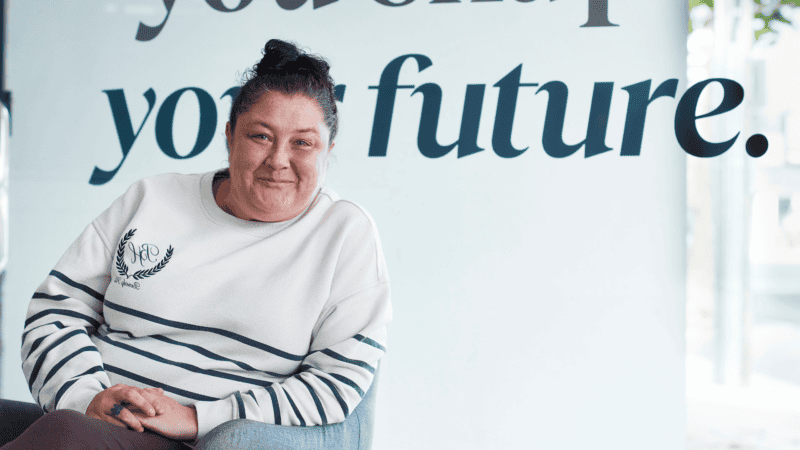 A woman sits smiling in a chair in front of the words &ldquo;your future.&rdquo;