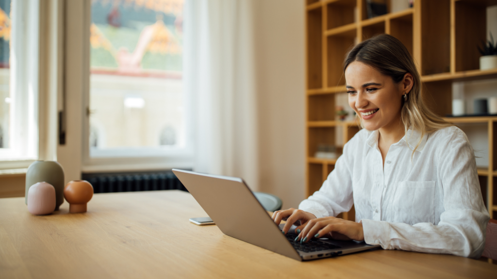 Smiling woman working on a laptop at a wooden table